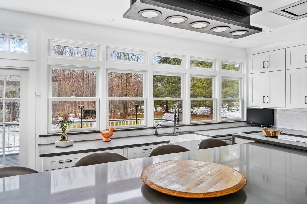 Transitional kitchen in Providence with a farmhouse sink, shaker cabinets, white cabinets, quartz benchtops, white splashback, subway tile splashback, stainless steel appliances, porcelain floors and with island.