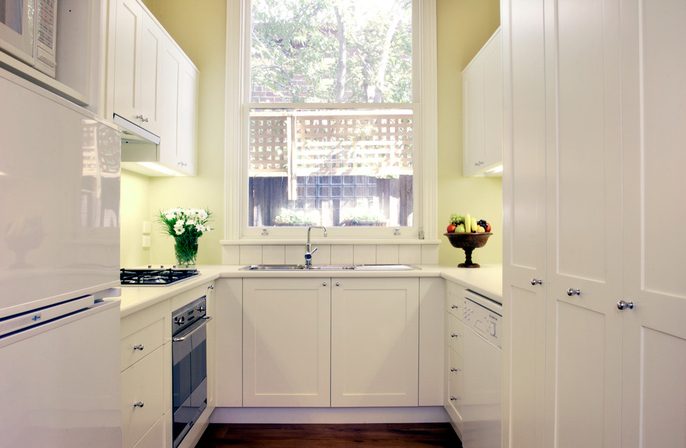 Inspiration for a small traditional u-shaped separate kitchen in Melbourne with a double-bowl sink, recessed-panel cabinets, white cabinets, white splashback, white appliances, light hardwood floors and no island.