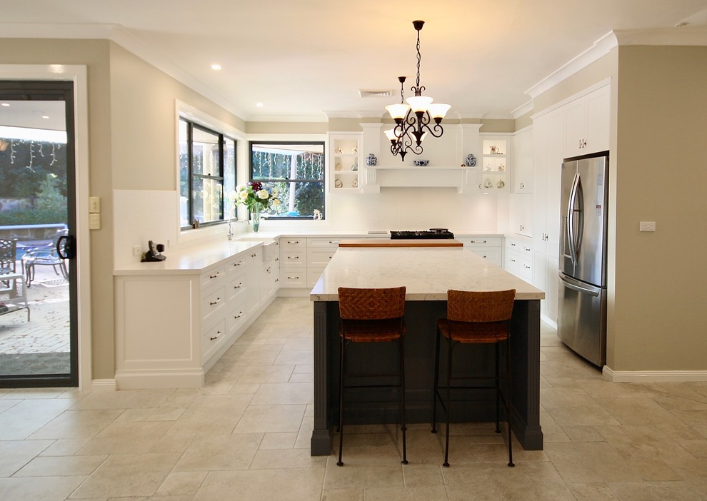 Photo of a mid-sized transitional u-shaped eat-in kitchen in Sydney with a farmhouse sink, shaker cabinets, white cabinets, quartz benchtops, white splashback, porcelain splashback, stainless steel appliances, porcelain floors, with island and beige floor.