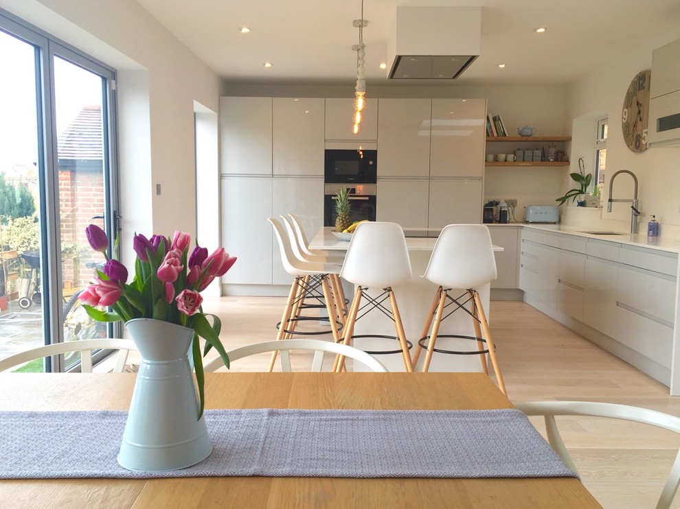 Photo of a scandinavian l-shaped eat-in kitchen in London with flat-panel cabinets, light hardwood floors, with island, white benchtop, an integrated sink, grey cabinets, limestone benchtops, white splashback, limestone splashback, panelled appliances and white floor.