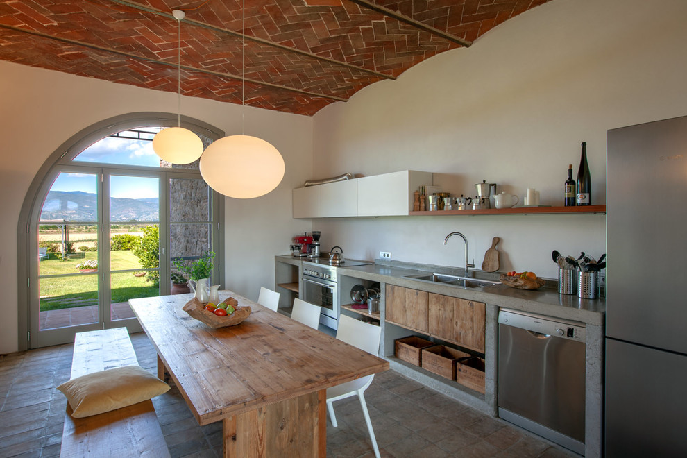 Mediterranean single-wall eat-in kitchen in Other with a drop-in sink, flat-panel cabinets, medium wood cabinets, concrete benchtops, stainless steel appliances, no island, brown floor and grey benchtop.