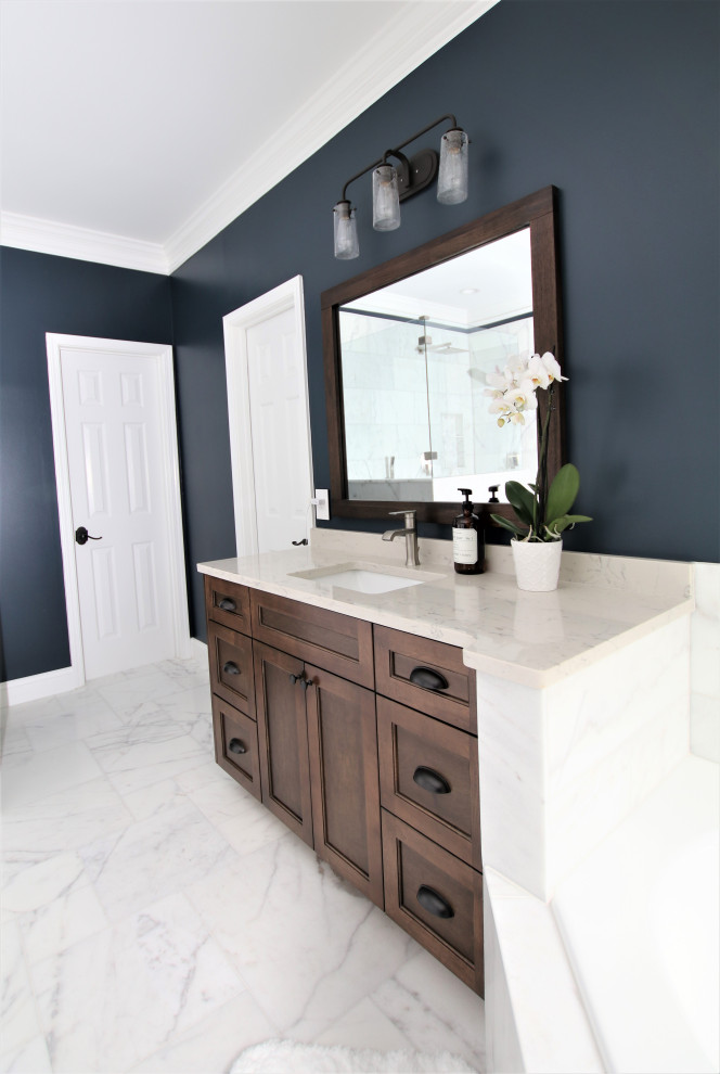 Large modern master bathroom in Atlanta with shaker cabinets, brown cabinets, a corner tub, a corner shower, white tile, marble, blue walls, marble floors, an undermount sink, engineered quartz benchtops, white floor, a hinged shower door and white benchtops.