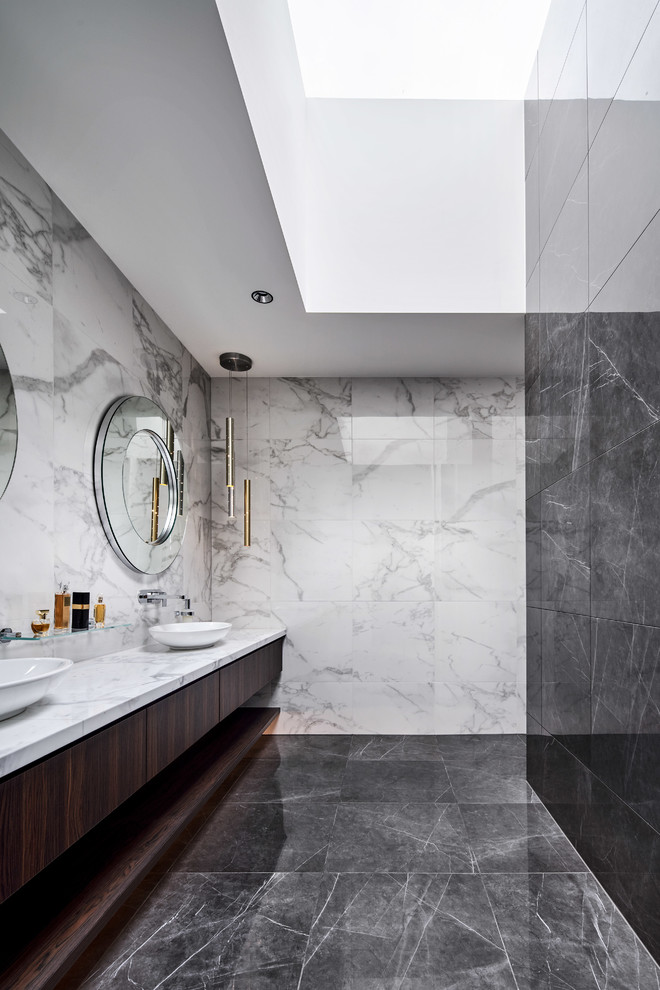 Design ideas for a large contemporary master bathroom in Melbourne with recessed-panel cabinets, dark wood cabinets, a freestanding tub, an open shower, a wall-mount toilet, white tile, marble, white walls, porcelain floors, a console sink, marble benchtops, grey floor, an open shower and white benchtops.