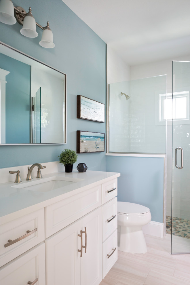 This is an example of a large beach style 3/4 bathroom in Tampa with shaker cabinets, white cabinets, an alcove shower, a one-piece toilet, blue walls, porcelain floors, an undermount sink, beige floor, a hinged shower door, white benchtops, a single vanity and a built-in vanity.