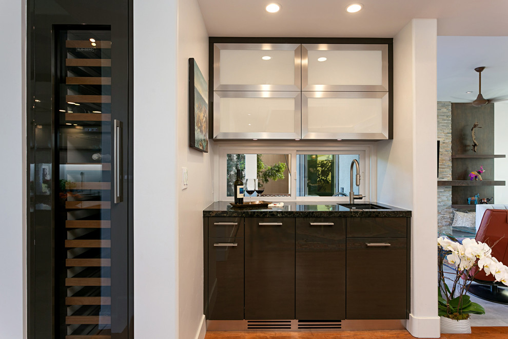 Photo of a small contemporary galley wet bar in San Diego with an undermount sink, glass-front cabinets, black cabinets, granite benchtops, medium hardwood floors, brown floor and black benchtop.