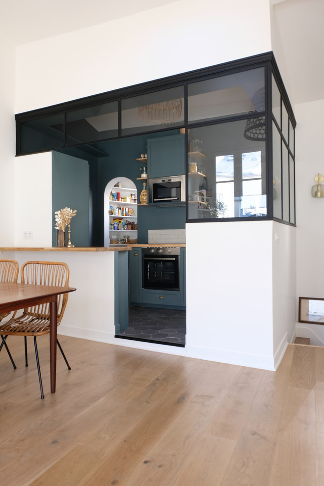 This is an example of a mid-sized industrial l-shaped open plan kitchen in Paris with green cabinets, wood benchtops, stainless steel appliances, ceramic floors, black floor, a single-bowl sink, beige splashback, terra-cotta splashback, with island and beige benchtop.