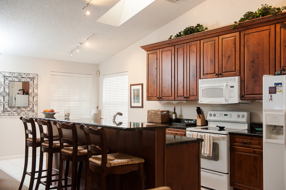 Inspiration for a large transitional galley ceramic tile eat-in kitchen remodel in Miami with an undermount sink, dark wood cabinets, granite countertops, white backsplash, white appliances and no island