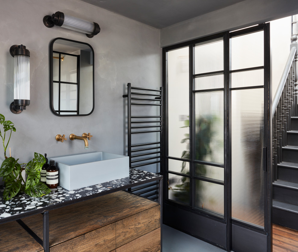 Photo of an industrial bathroom in London with flat-panel cabinets, dark wood cabinets, grey walls, a vessel sink, grey floors, black worktops, a single sink and a freestanding vanity unit.