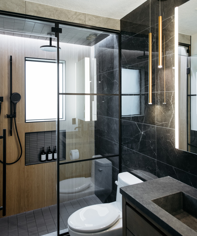 Inredning av ett modernt grå grått badrum med dusch, med släta luckor, en dusch i en alkov, en toalettstol med hel cisternkåpa, svart kakel, ett integrerad handfat, grått golv, dusch med gångjärnsdörr och skåp i mellenmörkt trä