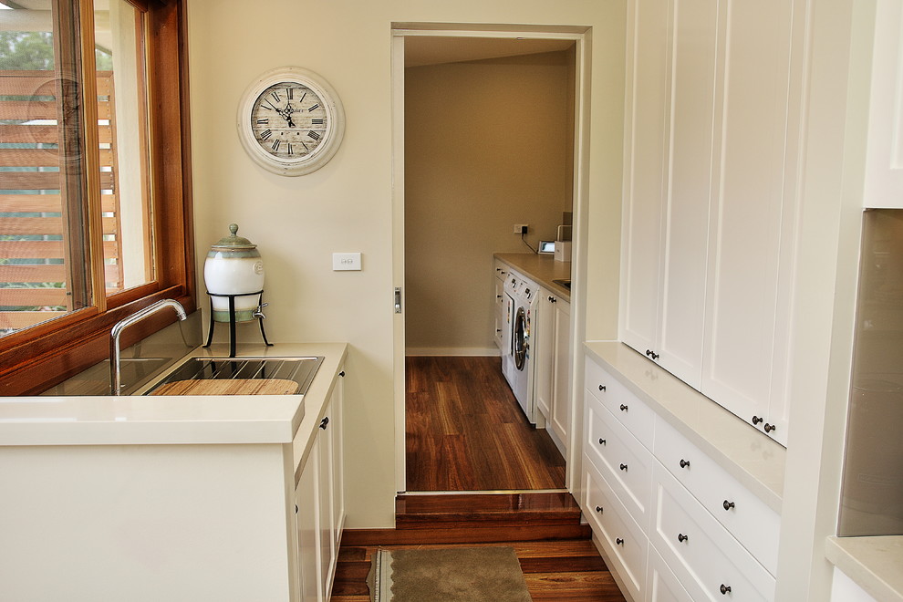 This is an example of a large traditional l-shaped kitchen pantry in Sydney with a drop-in sink, shaker cabinets, white cabinets, quartz benchtops, brown splashback, glass sheet splashback, stainless steel appliances, medium hardwood floors and with island.