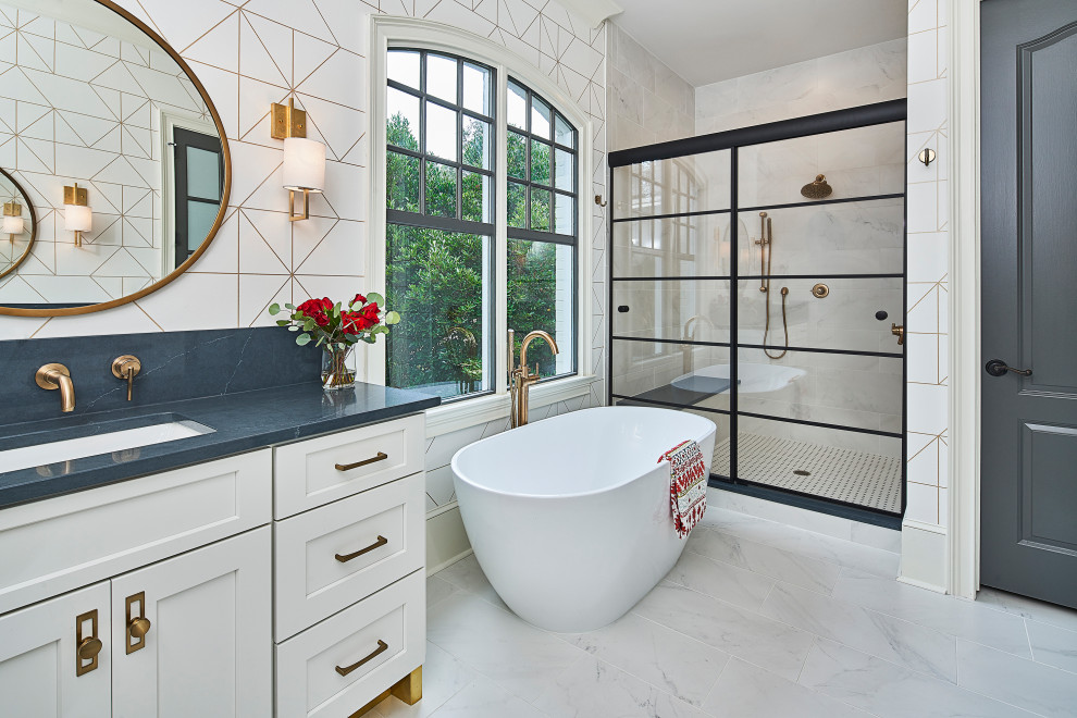 This is an example of a mid-sized transitional master bathroom in Charlotte with shaker cabinets, white cabinets, a freestanding tub, an alcove shower, white tile, porcelain tile, white walls, porcelain floors, an undermount sink, engineered quartz benchtops, white floor, a sliding shower screen and black benchtops.