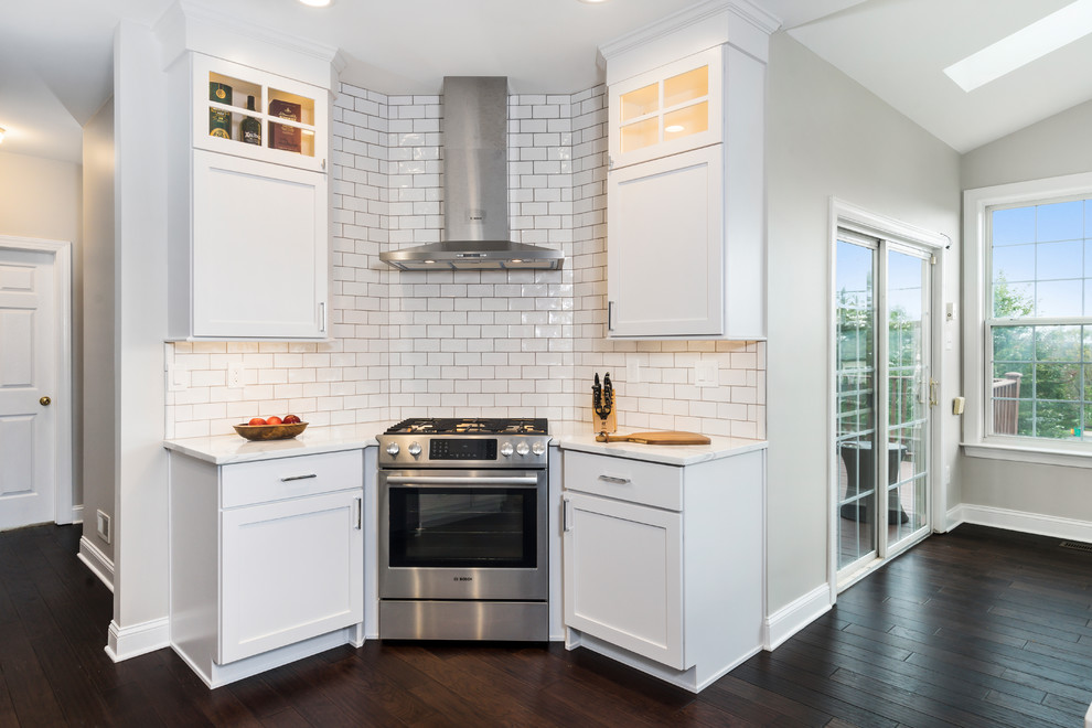 Inspiration for a large transitional l-shaped eat-in kitchen in Philadelphia with a farmhouse sink, shaker cabinets, white cabinets, quartz benchtops, white splashback, subway tile splashback, stainless steel appliances, dark hardwood floors, with island, brown floor and white benchtop.