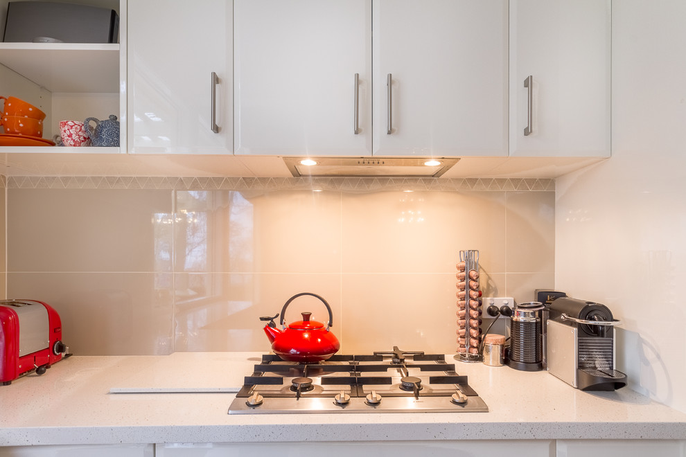 This is an example of a large contemporary l-shaped open plan kitchen in Sydney with an undermount sink, white cabinets, solid surface benchtops, beige splashback, ceramic splashback, stainless steel appliances, light hardwood floors and with island.