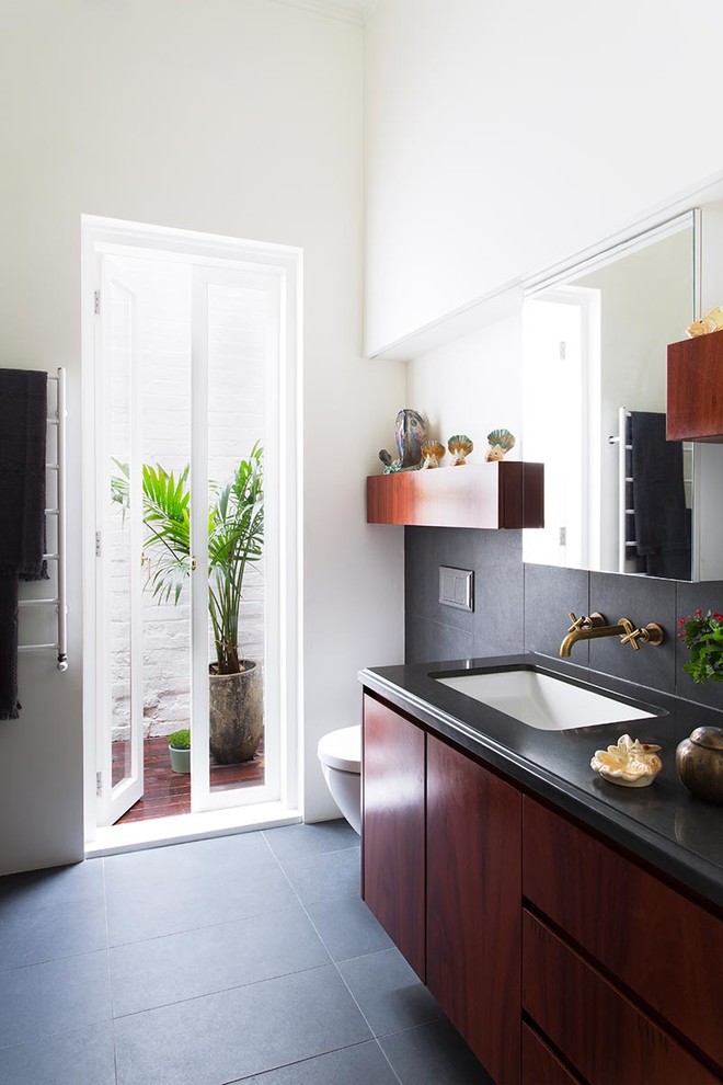 This is an example of a small contemporary master bathroom in Melbourne with an undermount sink, flat-panel cabinets, medium wood cabinets, solid surface benchtops, an open shower, a wall-mount toilet, multi-coloured tile, ceramic tile, white walls and concrete floors.