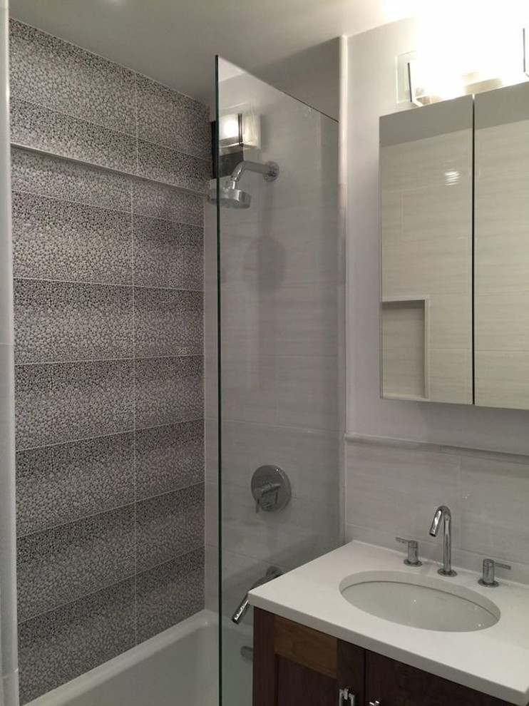 This is an example of a small contemporary 3/4 bathroom in New York with shaker cabinets, medium wood cabinets, an alcove shower, gray tile, grey walls, an undermount sink, solid surface benchtops and a hinged shower door.