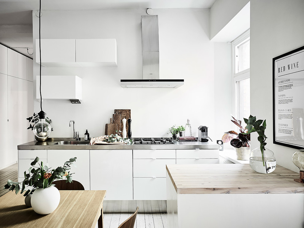 Photo of a small scandinavian single-wall eat-in kitchen in Gothenburg with a single-bowl sink, flat-panel cabinets, white cabinets, stainless steel benchtops, white appliances, painted wood floors and with island.