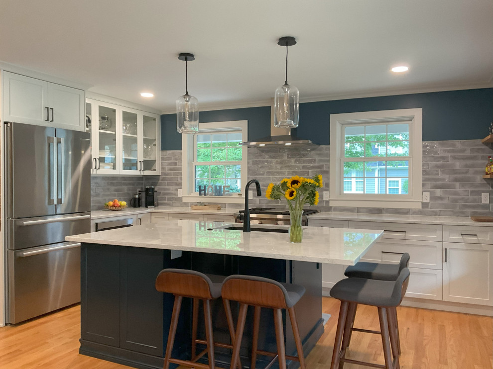 This is an example of a large transitional l-shaped eat-in kitchen in Detroit with an undermount sink, shaker cabinets, blue cabinets, quartz benchtops, grey splashback, cement tile splashback, stainless steel appliances, medium hardwood floors, with island, brown floor and white benchtop.