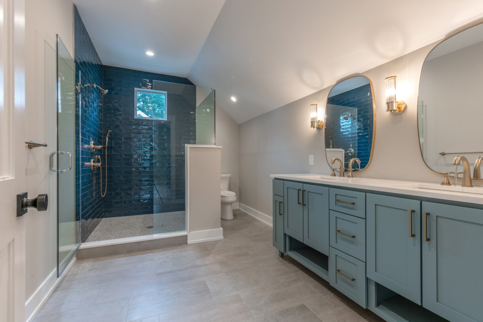 Cette image montre une grande salle d'eau rustique avec un placard à porte shaker, des portes de placard bleues, une douche d'angle, WC à poser, un carrelage beige, des carreaux de céramique, un mur beige, un sol en carrelage de porcelaine, un lavabo encastré, un plan de toilette en granite, un sol gris, une cabine de douche à porte battante, un plan de toilette blanc, une niche, meuble double vasque et meuble-lavabo encastré.