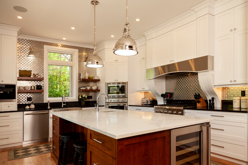 Example of a mid-sized transitional l-shaped enclosed kitchen design with shaker cabinets, white cabinets, stainless steel appliances, an island and white countertops