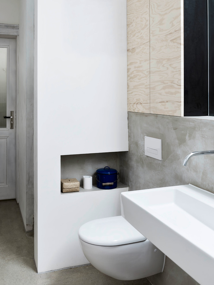 Design ideas for a small industrial powder room in Leipzig with a wall-mount toilet, white walls, concrete floors, a wall-mount sink and grey floor.