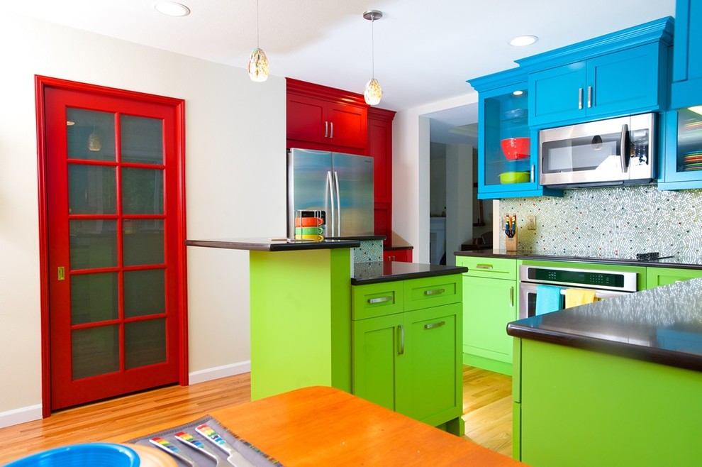 Design ideas for a mid-sized eclectic u-shaped eat-in kitchen in Seattle with an undermount sink, recessed-panel cabinets, red cabinets, quartz benchtops, multi-coloured splashback, glass tile splashback, stainless steel appliances, medium hardwood floors and with island.