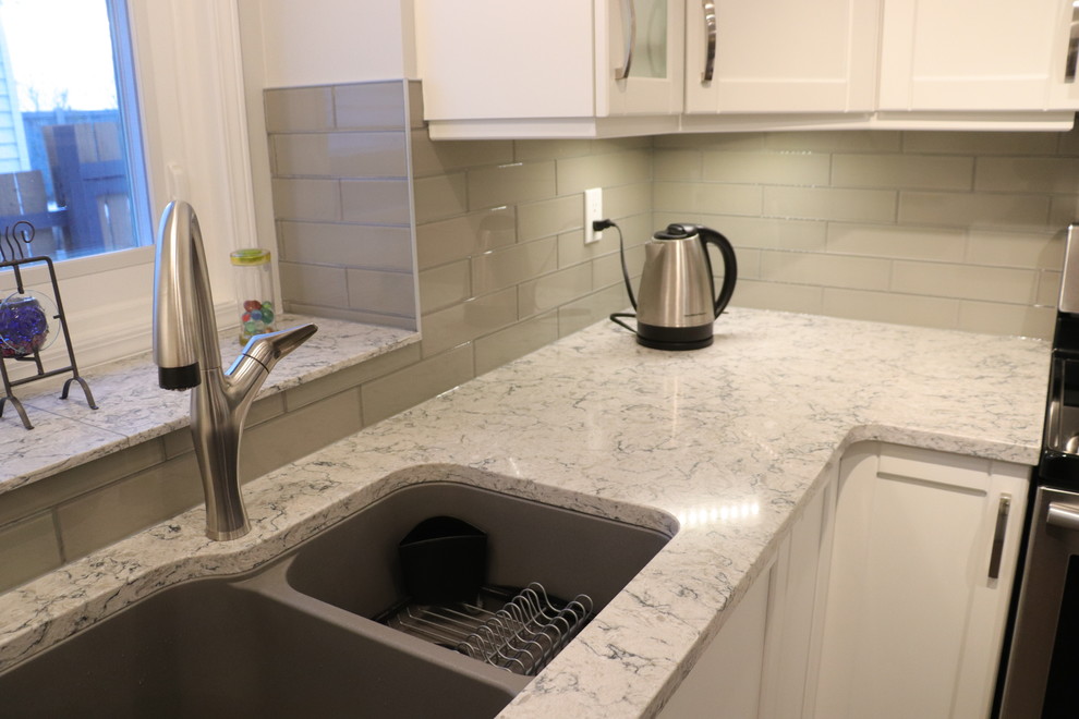 Example of a small transitional u-shaped eat-in kitchen design in Edmonton with an undermount sink, recessed-panel cabinets, white cabinets, quartz countertops, gray backsplash, glass tile backsplash, stainless steel appliances, no island and white countertops