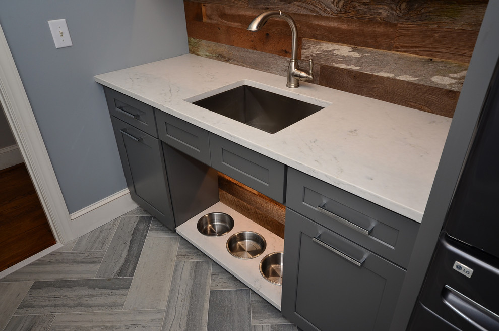 This is an example of a mid-sized country dedicated laundry room in Charlotte with an undermount sink, shaker cabinets, grey cabinets, quartz benchtops, blue walls, limestone floors and a stacked washer and dryer.