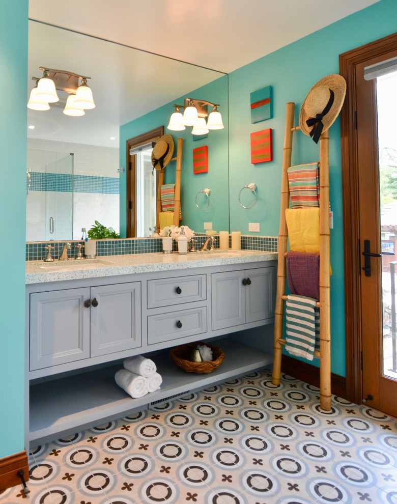 Photo of a mid-sized mediterranean kids bathroom in San Francisco with furniture-like cabinets, grey cabinets, a drop-in tub, an alcove shower, a two-piece toilet, blue tile, glass sheet wall, blue walls, cement tiles, an undermount sink, recycled glass benchtops, blue floor and a hinged shower door.