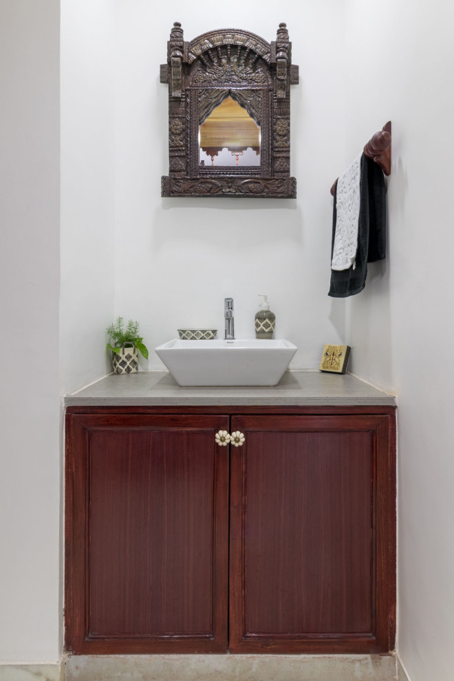 This is an example of a small traditional powder room in Ahmedabad with recessed-panel cabinets, medium wood cabinets, white walls, a vessel sink, grey floor, grey benchtops and a built-in vanity.