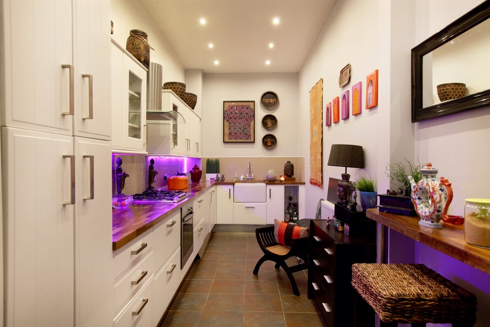 This is an example of a large traditional galley eat-in kitchen in Other with an integrated sink, louvered cabinets, white cabinets, wood benchtops, beige splashback, mosaic tile splashback, black appliances and slate floors.
