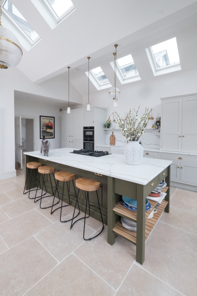 This is an example of a large traditional single-wall open plan kitchen in Cardiff with a farmhouse sink, shaker cabinets, light wood cabinets, quartzite benchtops, white splashback, stone slab splashback, stainless steel appliances, porcelain floors, with island, white benchtop and vaulted.