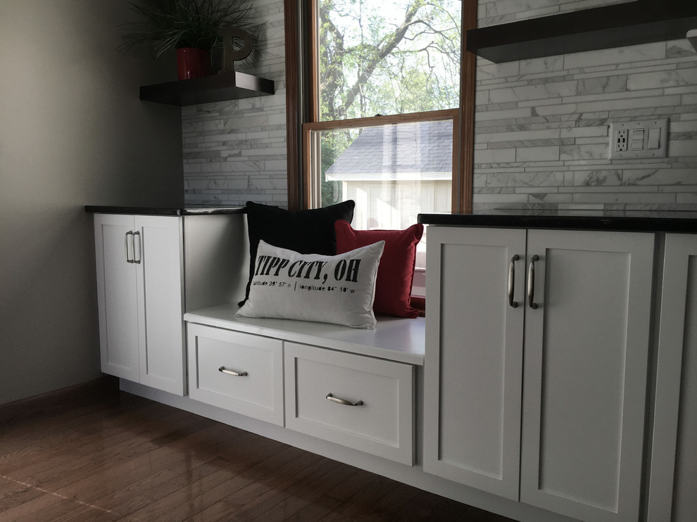 Inspiration for a large transitional single-wall medium tone wood floor eat-in kitchen remodel with an undermount sink, shaker cabinets, white cabinets, granite countertops, multicolored backsplash, marble backsplash, stainless steel appliances, an island and black countertops