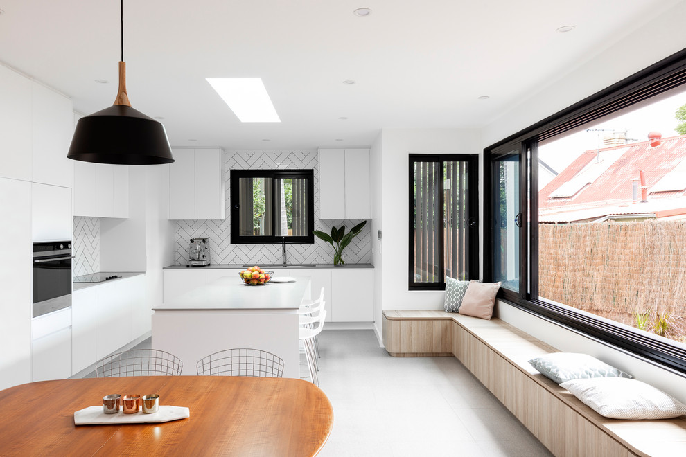 Contemporary l-shaped eat-in kitchen in Sydney with white cabinets, subway tile splashback, with island, grey floor, grey benchtop, flat-panel cabinets and white splashback.