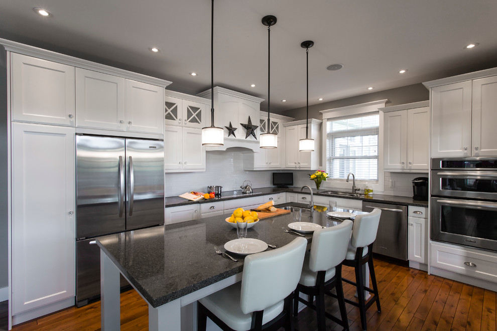 This is an example of a traditional l-shaped kitchen in Toronto with shaker cabinets, white cabinets, white splashback, subway tile splashback and stainless steel appliances.