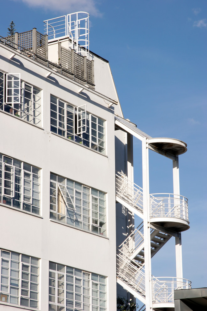 This is an example of a large industrial three-storey stucco white apartment exterior in London with a flat roof.