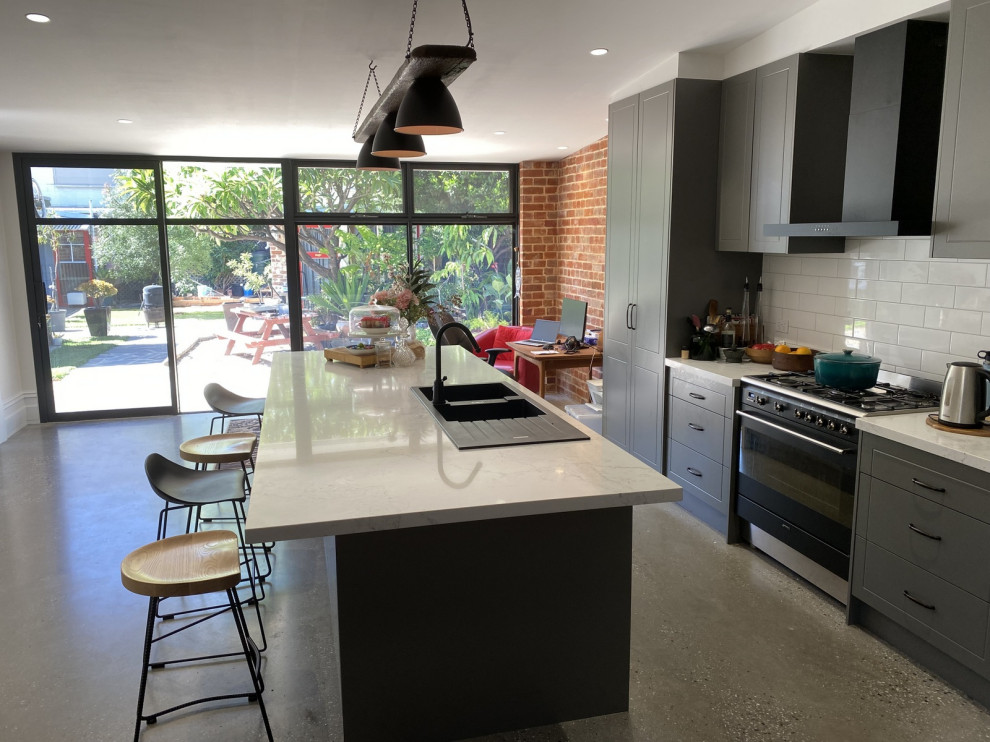 Design ideas for a mid-sized modern galley open plan kitchen in Adelaide with a double-bowl sink, shaker cabinets, grey cabinets, quartz benchtops, white splashback, ceramic splashback, black appliances, terrazzo floors, with island, beige floor and white benchtop.