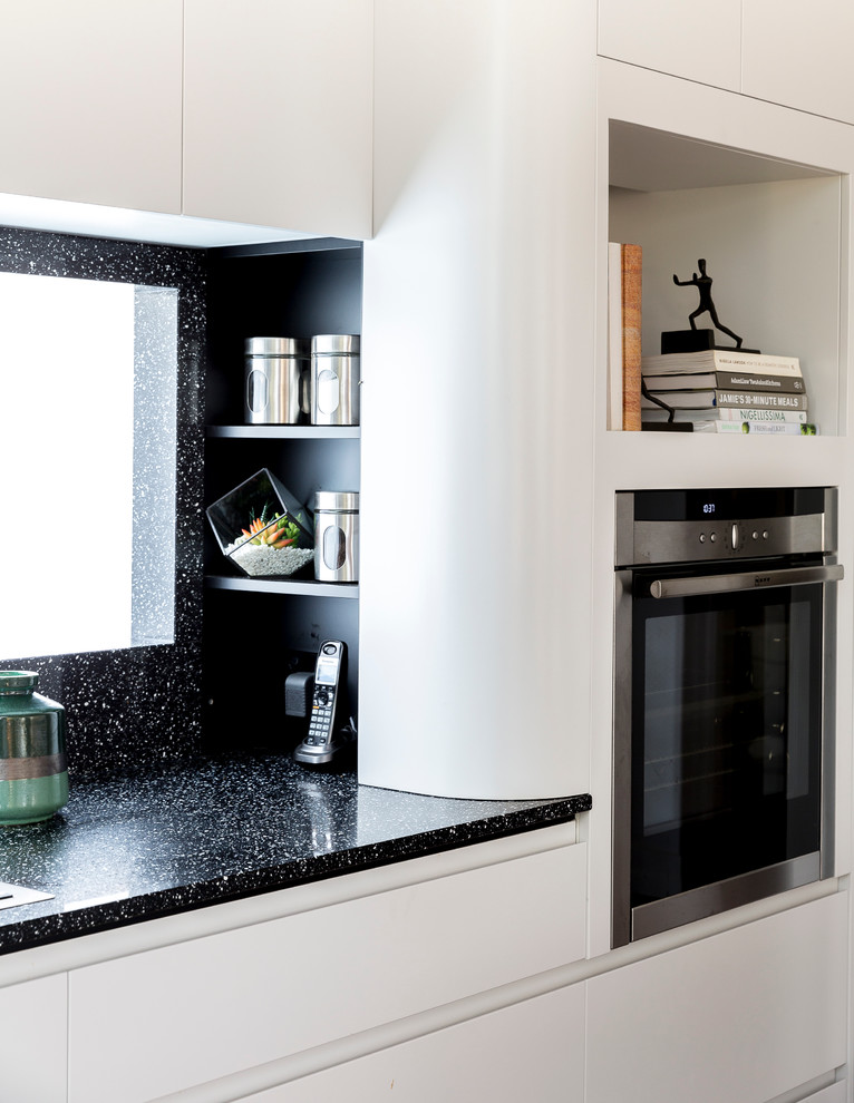 Photo of a contemporary l-shaped kitchen in Brisbane with white cabinets, quartz benchtops, black splashback, medium hardwood floors and with island.