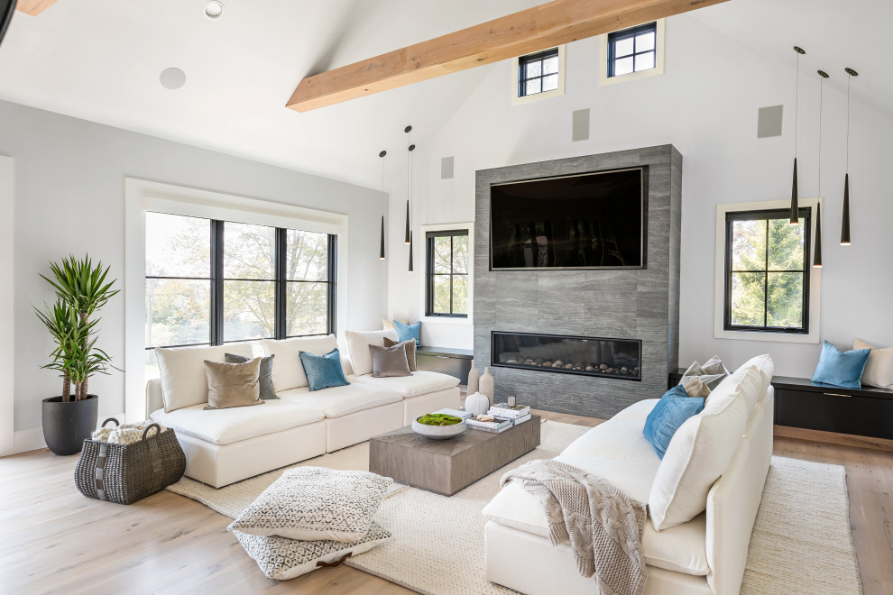 Expansive contemporary open plan games room in New York with white walls, light hardwood flooring, a standard fireplace, a stone fireplace surround, a built-in media unit, beige floors and a vaulted ceiling.