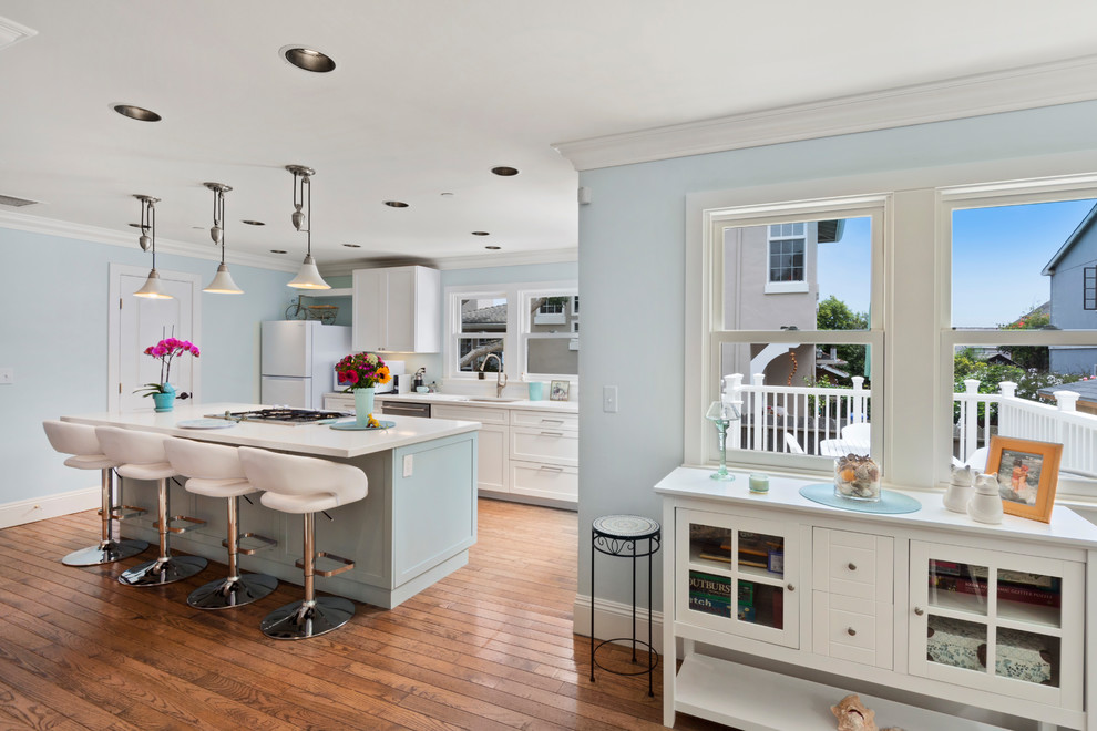 Design ideas for a mid-sized beach style galley open plan kitchen in Other with a single-bowl sink, shaker cabinets, turquoise cabinets, quartz benchtops, white splashback, stainless steel appliances, medium hardwood floors, with island, brown floor and white benchtop.