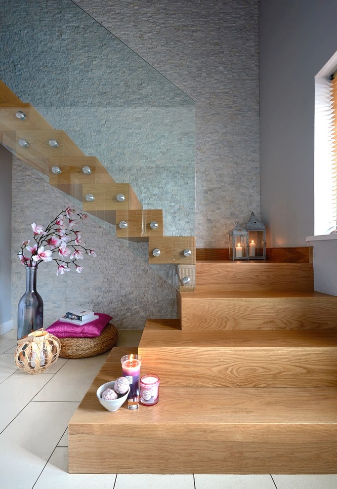 This is an example of a large contemporary wood floating staircase in West Midlands with wood risers and glass railing.