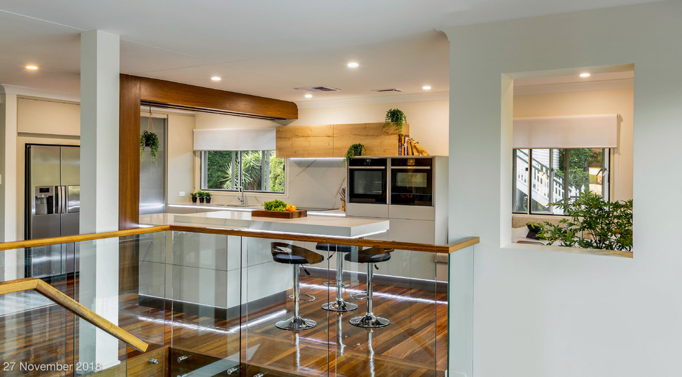 Design ideas for a large contemporary l-shaped eat-in kitchen in Brisbane with an undermount sink, flat-panel cabinets, beige cabinets, quartz benchtops, white splashback, stone slab splashback, black appliances, medium hardwood floors, with island, multi-coloured floor and yellow benchtop.