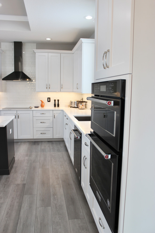 This is an example of a large transitional l-shaped open plan kitchen in Other with an undermount sink, flat-panel cabinets, white cabinets, quartz benchtops, white splashback, glass tile splashback, black appliances, vinyl floors, with island, grey floor, white benchtop and recessed.