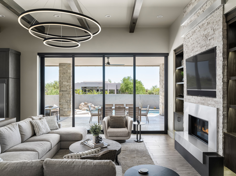 Inspiration for a large mediterranean open concept family room in Phoenix with a library, beige walls, ceramic floors, a standard fireplace, a stone fireplace surround, a wall-mounted tv and brown floor.
