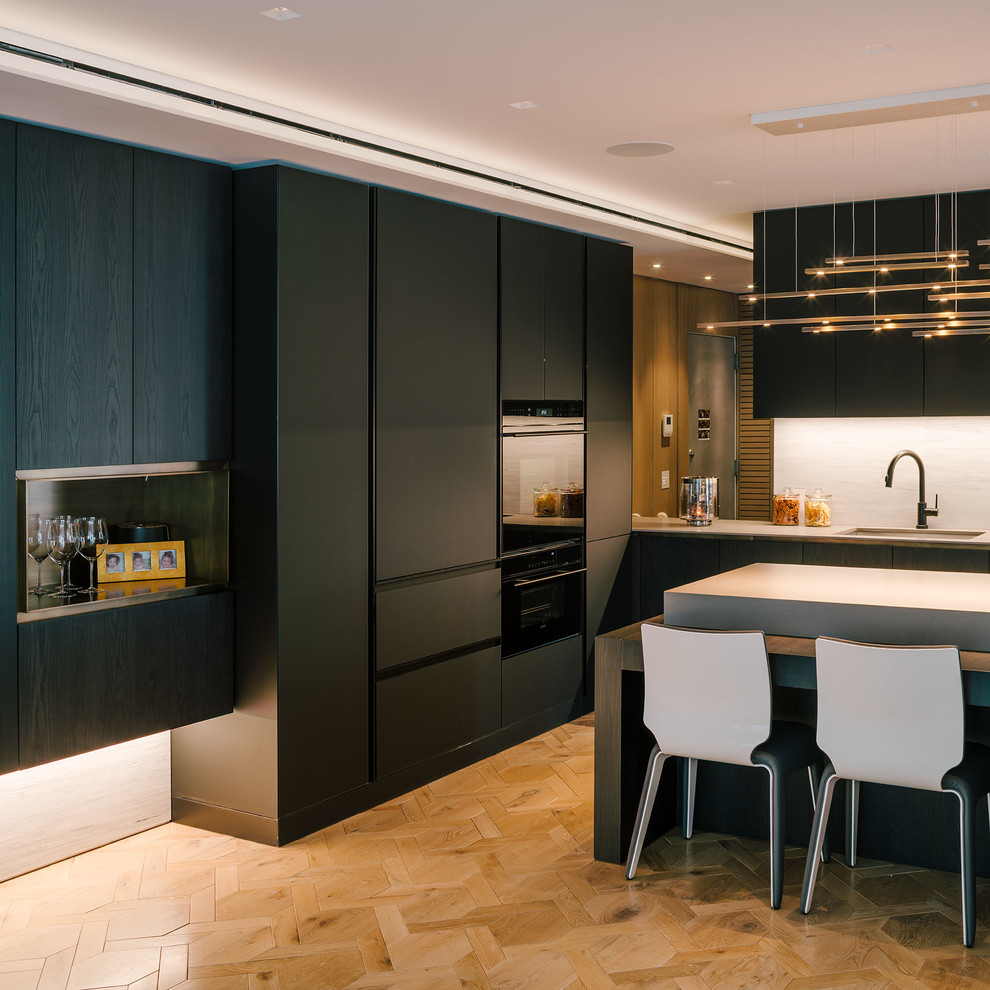 Photo of a large modern single-wall open plan kitchen in New York with an undermount sink, flat-panel cabinets, black cabinets, concrete benchtops, grey splashback, stone slab splashback, black appliances, light hardwood floors, with island and beige floor.