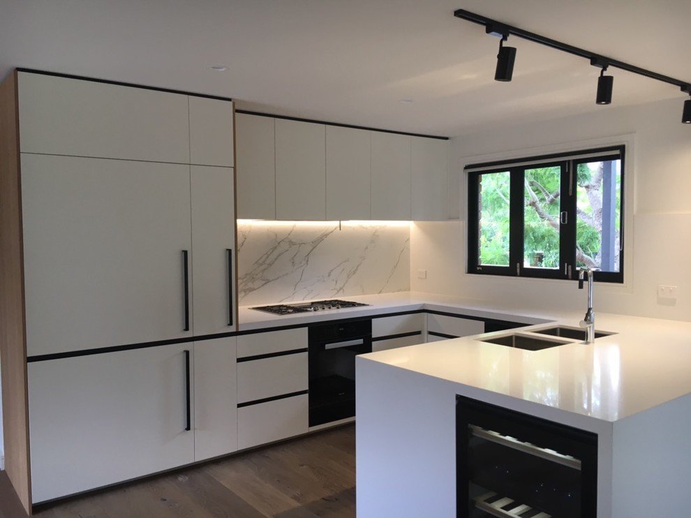 Inspiration for a mid-sized contemporary u-shaped open plan kitchen in Melbourne with an undermount sink, white cabinets, quartz benchtops, white splashback, marble splashback, black appliances, medium hardwood floors, with island and brown floor.
