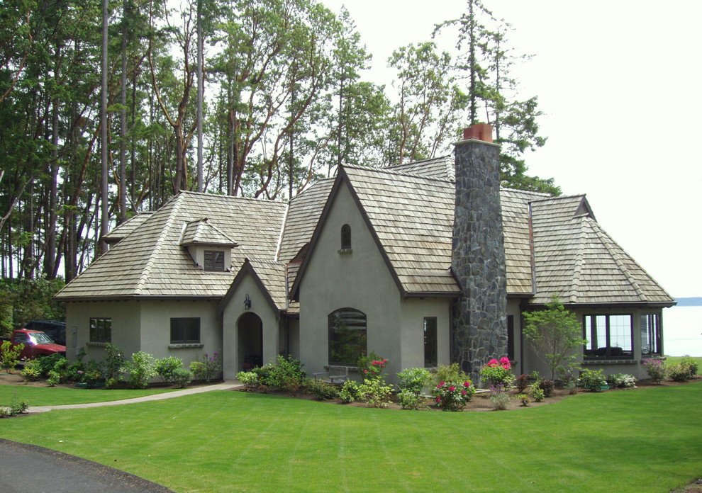 This is an example of a large traditional one-storey stucco green house exterior in Seattle with a gable roof and a shingle roof.