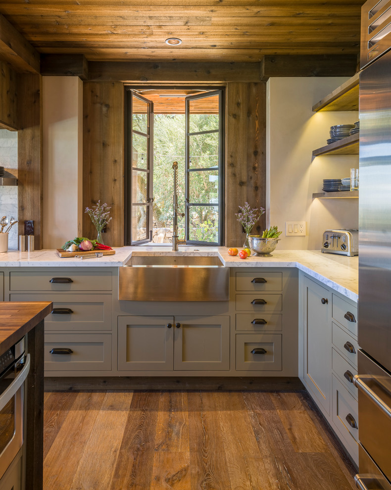 This is an example of a mid-sized country l-shaped kitchen in San Francisco with a farmhouse sink, grey cabinets, marble benchtops, stainless steel appliances, medium hardwood floors and window splashback.