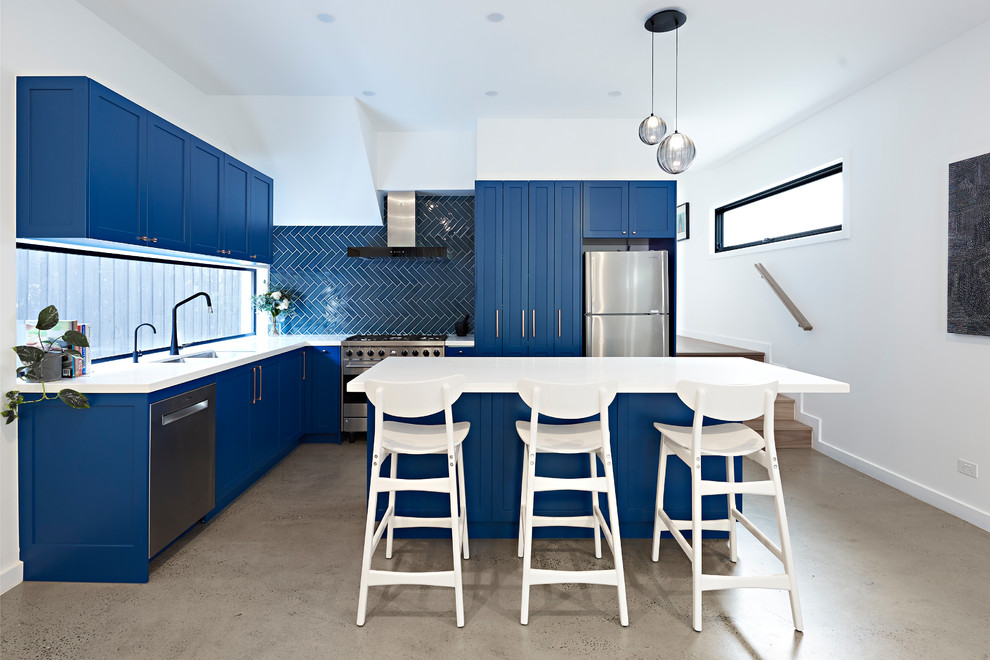 Mid-sized transitional l-shaped kitchen in Melbourne with a double-bowl sink, shaker cabinets, blue cabinets, blue splashback, stainless steel appliances, with island, white benchtop, ceramic splashback, concrete floors, grey floor and quartz benchtops.