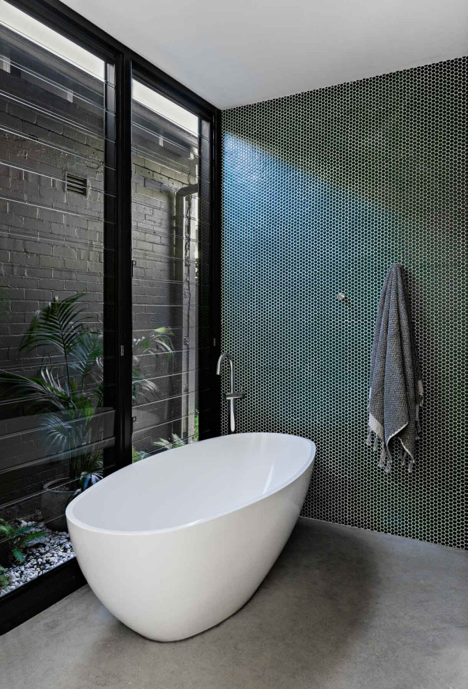 Пример оригинального дизайна: главная ванная комната среднего размера в стиле модернизм с плоскими фасадами, светлыми деревянными фасадами, отдельно стоящей ванной, душем в нише, унитазом-моноблоком, зеленой плиткой, керамической плиткой, белыми стенами, бетонным полом, монолитной раковиной, столешницей из искусственного камня, серым полом, открытым душем, белой столешницей, тумбой под две раковины и подвесной тумбой