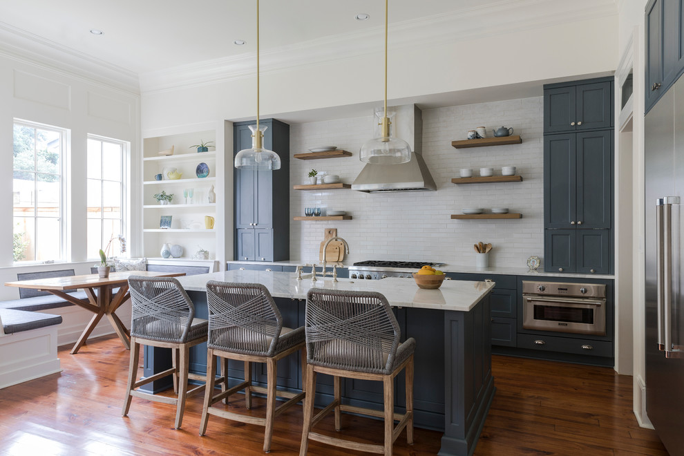 Inspiration for a transitional l-shaped eat-in kitchen in New Orleans with a farmhouse sink, shaker cabinets, grey cabinets, white splashback, subway tile splashback, stainless steel appliances, medium hardwood floors, with island, brown floor, white benchtop and marble benchtops.
